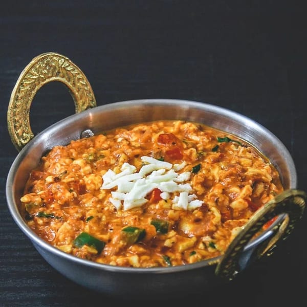 A close-up of Indian paneer bhurji, a scrambled paneer dish, in a traditional metal serving bowl.