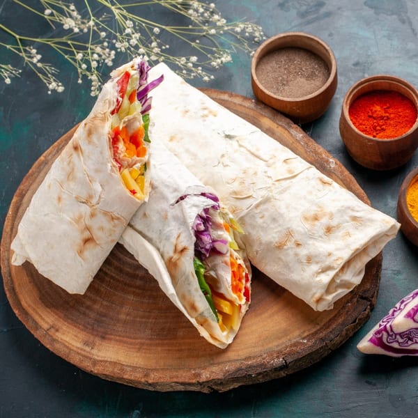 Three Curry Nation wraps with colorful fillings on a wooden board, with spices in bowls.